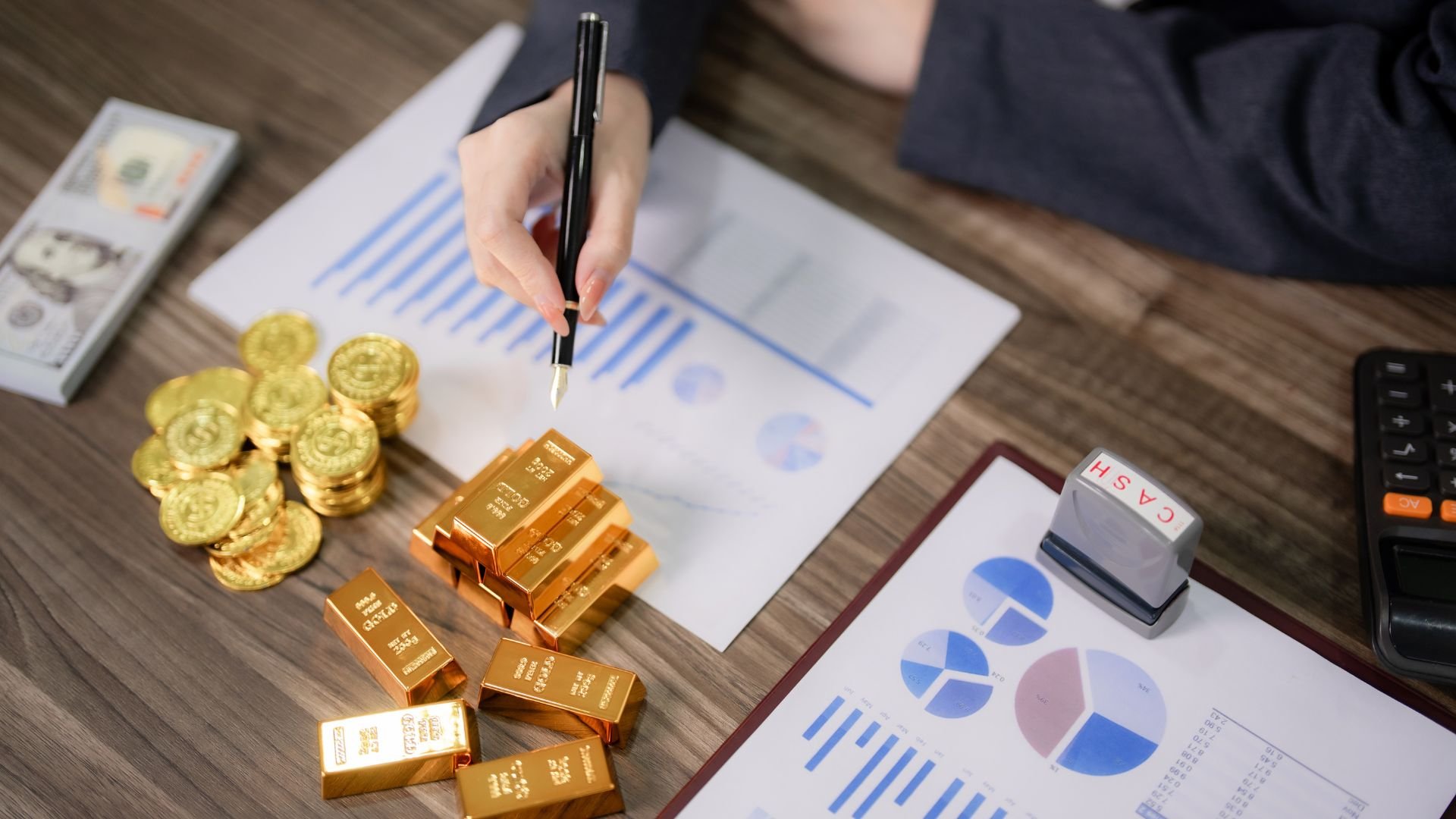 Gold bars and coins with financial charts and hand analyzing investment data